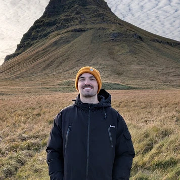 Rubén Moya sonriendo, con gorro naranja y chaqueta negra, con una montaña al fondo